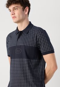 Námornícky polo tričko s mriežkovaným vzorom, s golierom a krátkymi rukávmi. Stredová nášivka s logom dodáva detail. Mäkký bavlnený materiál.
