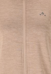 Beige zip-jakke med struktureret overflade, med en kontrasterende lynlås og et lille logo på den øverste højre side.