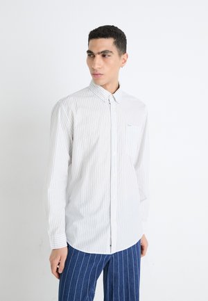 Chemise blanche à col avec des rayures verticales grises claires, dotée d'une poche poitrine, fabriquée dans un tissu lisse.