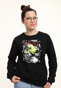 Morbido felpa nera con grafica di un fantasma in stile cartone animato di colore verde, con macchie bianche e testo colorato. Polsini a costine e collo rotondo.