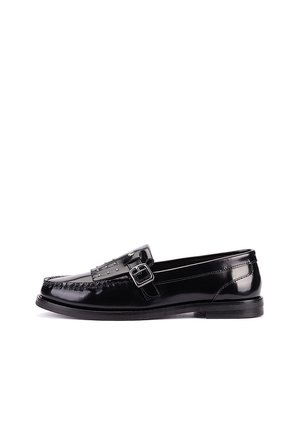 Mocasín de cuero negro brillante con hebilla plateada y pequeños remaches en la correa, visto de lado sobre un fondo blanco.
