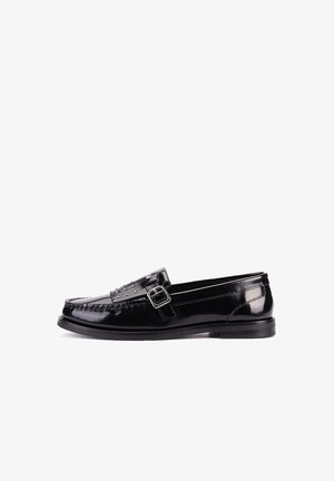 Mocasín de cuero negro brillante con hebilla plateada y pequeños remaches en la correa, visto de lado sobre un fondo blanco.