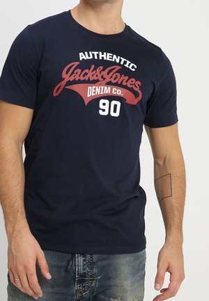 T-shirt en coton bleu marine avec un imprimé graphique rouge et blanc indiquant "AUTHENTIC Jack & Jones DENIM CO 90." Col rond.