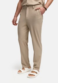 Beige geribde broeken met een getailleerde pasvorm, voorzien van zijzakken en een ceintuurlus, gecombineerd met witte sandalen. Soepele textuur en verticale patroon.