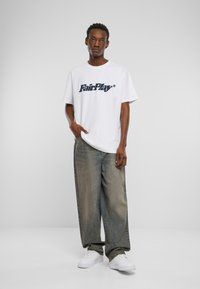 Hvid bomulds t-shirt med "FairPlay" logo i mørkeblå, parret med løstsiddende, lysede jeans og hvide sneakers. Enkel design, afslappet pasform.
