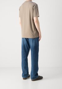 Hnědý bavlněný tričko s kulatým výstřihem, kombinované s volnými modrými džínami. Džíny mají klasický pětikapsový design.