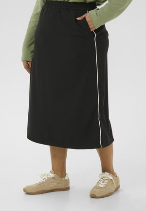 Zwarte midi-rok met een elastische tailleband en witte zijkanten. Gepaarde met lichtbruine sneakers met een suède textuur en witte accenten.