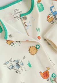 Unisex baba body krémszínű pamutból, zöld díszítéssel és vidám farmtémájú illusztrációkkal, beleértve egy tehenet, napot és zöldségeket.