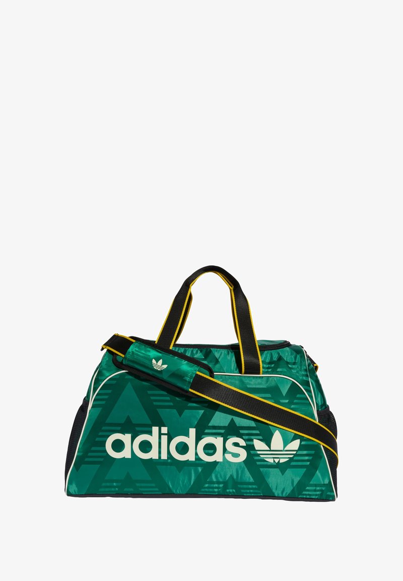 Zielona torba sportowa z białym logo Adidas, geometrycznym wzorem, czarnymi akcentami i żółtym paskiem. Wykonana z trwałego materiału, wyposażona w krótkie uchwyty.