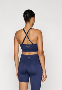 Granatowy zestaw odzieży sportowej z krzyżowanym tyłem w biustonoszu sportowym oraz wysokim stanem szortów. Gładka faktura z subtelnym logo na obu elementach.