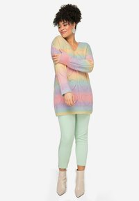Maglione lavorato a maglia con scollo a V, strisce arcobaleno pastello con motivi a cuore, abbinato a leggings verde menta e stivali con tacco color beige.