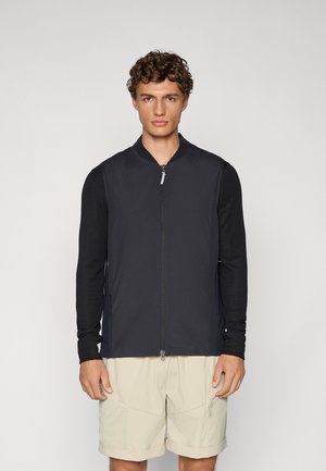 Black bomber-style jacket with a front zipper, long sleeves, and a smooth texture, paired with light beige shorts.
