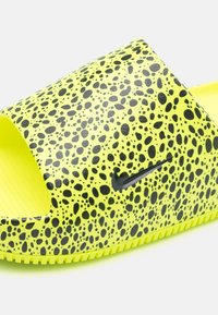 Nike žabky s jasně žlutým svrškem, který zdobí tečkovaný černý vzor, otevřeným designem špičky a texturovanou stélkou pro lepší přilnavost.
