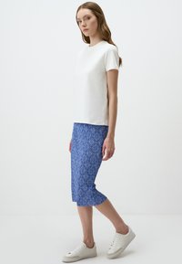 T-shirt blanc à manches courtes, jupe crayon bleue à motifs et baskets blanches. La jupe présente des motifs bleus intriqués sur une surface texturée.