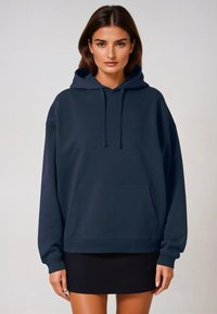 Felpa oversized color blu navy realizzata in tessuto morbido, con una grande tasca frontale e cappuccio con cordino. Abbinata a una gonna nera.