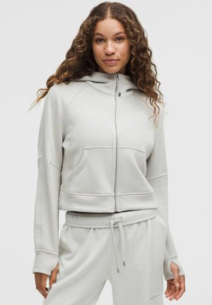 Hanorac scurt de culoare gri deschis, cu fermoar complet, buzunare tip kangur și manșete din tricot. Disponibil cu glugă și fabricat dintr-un material moale, texturat.