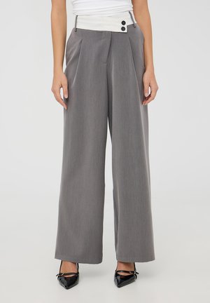 Pantaloni a gamba larga grigi realizzati in tessuto texturizzato con una vita bianca dotata di due bottoni. Abbinati a scarpe nere con punta.