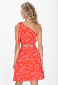 Punase ja roosa troopilisest lehekujust koosneva lühikese ülaosa ühe õlapaelaga, millele on lisatud sobiv seelik, millel on kogutud vöökoht.