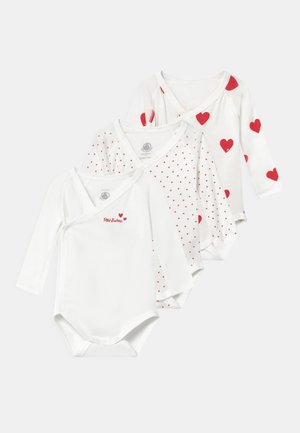 Tres bodies blancos de bebé con mangas largas: uno con corazones rojos, uno con pequeños corazones rojos y uno que presenta "Petit Bateau" en texto rojo.