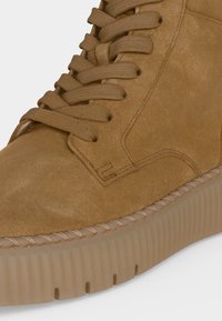 Gros plan d'une basket en daim beige avec une semelle épaisse en caoutchouc, un bout rond et des lacets épais assortis passés dans des œillets métalliques.
