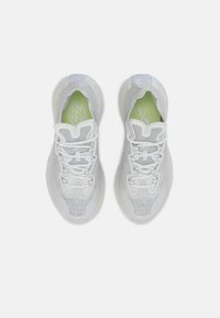 Ett par vita mesh-sneakers med unikt rutmönster och gröna innersulor, visade från ovan mot en ljusgrå bakgrund.