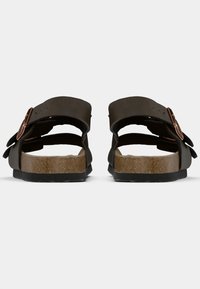 Brown cork-soled sandals with two wide straps, adjustable buckles, and open back design. Matte finish and textured surface.