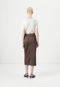 Brun denim midi-skjørt med to baklommer, kontrasterende søm og en tettsittende midje. Kombinert med en lys beige t-skjorte og svarte hæler.