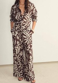 Combinaison à motifs marron et crème avec manches longues, col et ceinture élastique ; présente une coupe ample et des jambes larges.