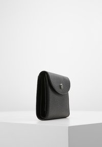 Portafoglio in pelle nera testurizzata con patta arrotondata, chiusura a pressione in essere e più scomparti, esposto in posizione verticale su una superficie bianca.