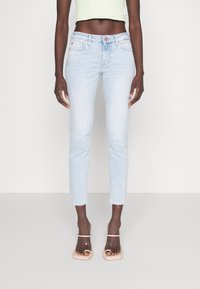 Hellblaue, figurbetonte Jeans mit fransigem Saum, fünf Taschen und Knopfverschluss, kombiniert mit klaren Sandalen mit Absatz.