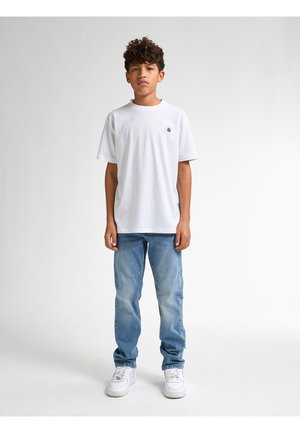 T-shirt en coton blanc à manches courtes, encolure ronde, avec un petit logo noir sur la poitrine, associée à un jean en denim bleu clair et des baskets blanches.