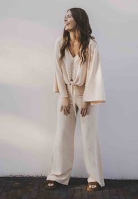 Beige tweed set met een knooptrui met lange mouwen en losvallende, wijde broek. Glad textiel.