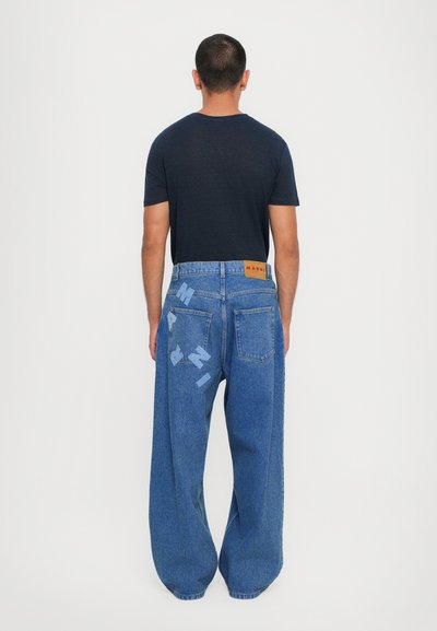 Baggy denimjeans i ljusblått med en etikett på bakslutet. Påfallande textakcenter i en mörkare blå på bakfickorna.