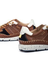 Zapatillas de cuero marrón con paneles de malla, detalles en blanco y marino, lengüeta amarilla en el talón y suela de goma gris moteada. Detalles de costura en los laterales.