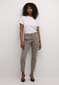 Helle graue Chinos im Slim Fit, mit Gürtelschlaufen und Fronttaschen, kombiniert mit einem schlichten weißen T-Shirt und schwarzen Highheels.