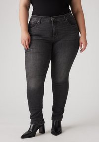 Zwarte skinny jeans van denim met subtiele vervaging en versleten accenten. Hoge taille met zijzakken. Gepaard met zwarte haklaarzen.