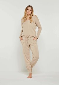 Beige Strickpullover mit V-Ausschnitt und gerippter Textur, kombiniert mit passenden, schmal zulaufenden Jogginghosen mit Kordelzug und seitlichen Taschen.