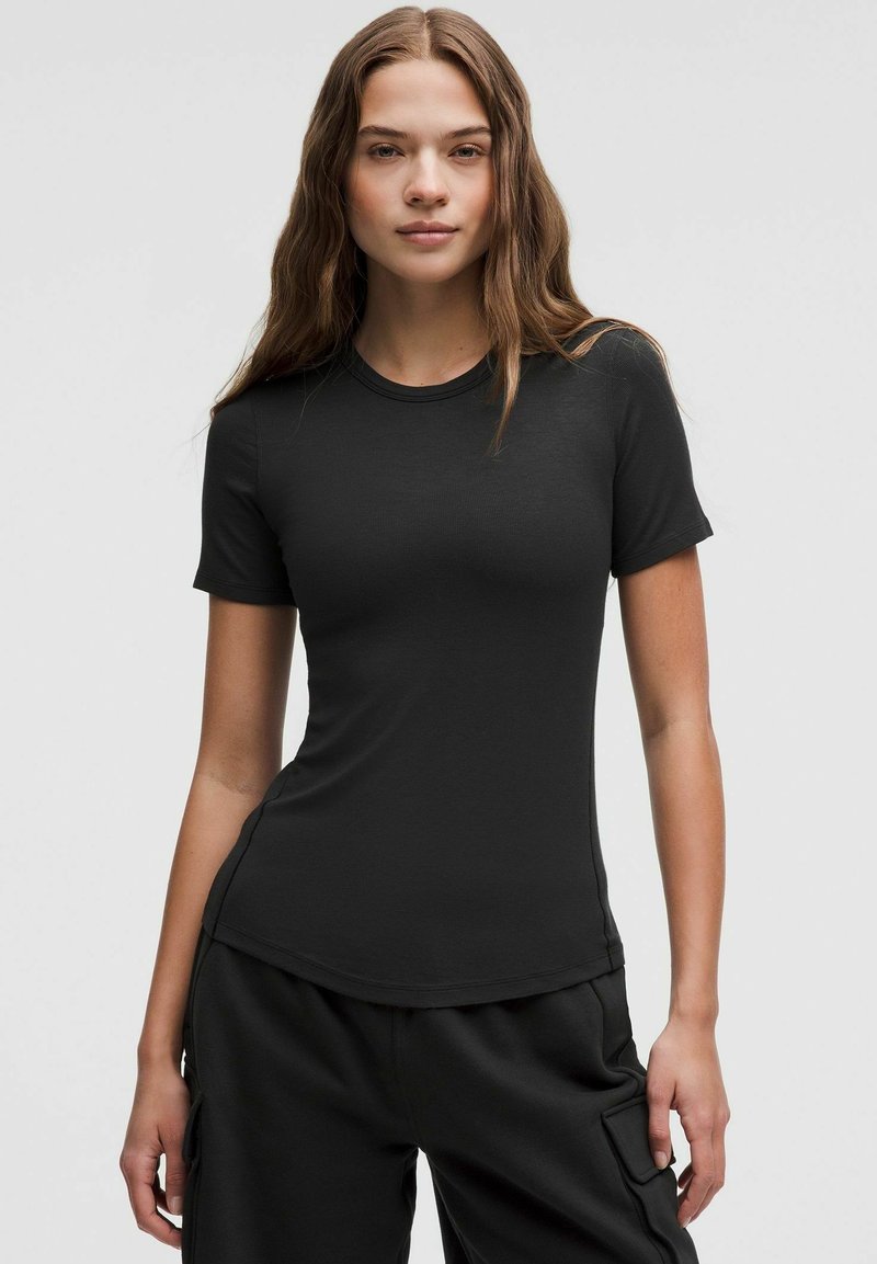 Tricou negru, cu un croi ajustat, mâneci scurte, decolteu rotund, textură fină și un tiv ușor curbat, asortat cu pantaloni negri, lejeri.