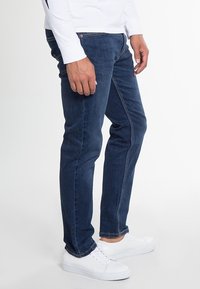 Mörkblå denimjeans med smal passform, med sydda detaljer, framfickor och en slät yta; bärs med vita sneakers.