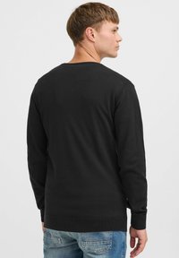 Black long-sleeve sweatshirt with a crew neck, featuring a smooth texture and ribbed cuffs. Worn with light blue jeans, showcasing a simple design.