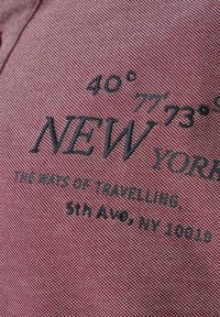 Bordowa tkanina z teksturowanym wzorem; zawiera czarny haftowany tekst z detalami koordynatów i lokalizacji. Akcenty obejmują logo "NOWY JORK".