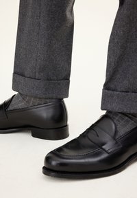 Czarne skórzane loafersy o gładkim wykończeniu, kontrastujące szare skarpetki w wzory oraz szare spodnie z zagiętymi mankietami, prezentujące dopasowany krój.