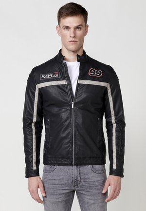 Chaqueta de moto de cuero negro con rayas plateadas, cremallera frontal, cuello alto y parches bordados con los números 99 y KRS.01.
