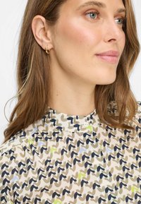 Overhemd met knoopjes, met een crèmekleurige achtergrond en abstracte patronen in bruin, blauw en groen; hoge kraag en een enkele knoopdetail.