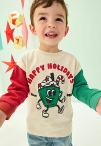 Lange mouw shirt in crème met rode en groene mouwen. Bevat een groene drinkpersoonlijkheid en de tekst "VROLIJKE FEESTDAGEN" in het rood. Casual stijl.