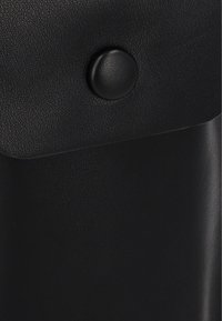 Czarna torba z fakturowanej skóry z klapką, z okrągłym magnesem zatrzaskowym i gładkimi krawędziami, zapewniającymi czysty design.