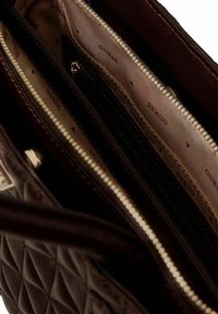 Borsa trapuntata marrone con chiusura a zip. L'interno presenta più scomparti foderati con tessuto beige e il logo del marchio ripetuto.