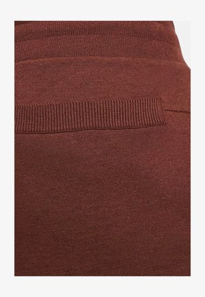 Tissu bordeaux avec une texture lisse et une ceinture côtelée. Des lignes horizontales subtiles dans le motif tricoté créent un intérêt visuel.