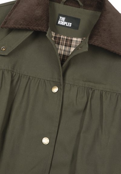 Chaqueta verde oliva de tela con detalles plisados, cuello de pana marrón y forro con patrón a cuadros. Cuenta con cierre de botones a presión metálicos.