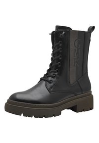 Bottines en cuir noir avec un laçage à l'avant, semelle rainurée et panneau en tissu présentant le texte "GMK". Design épais et durable.